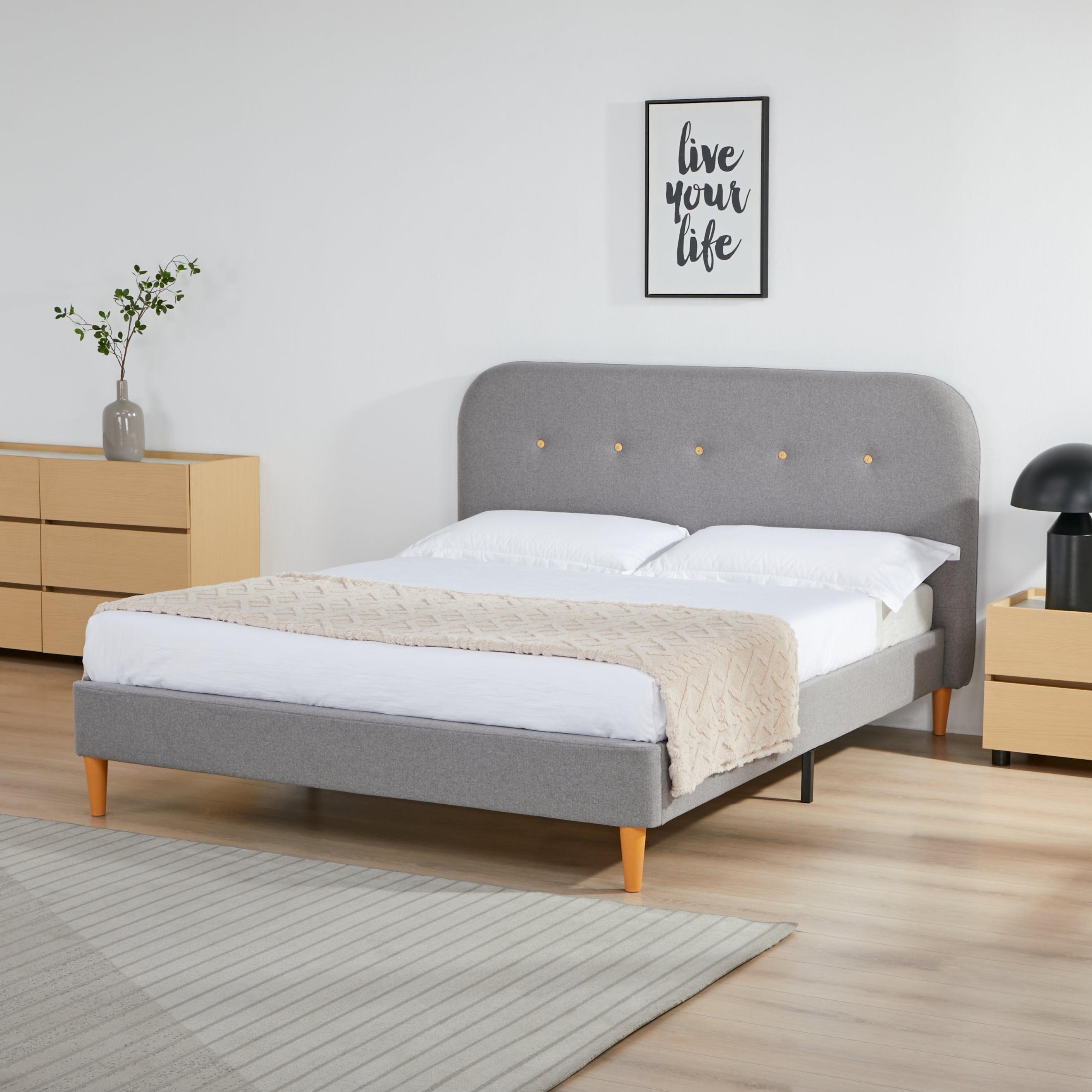 Gray upholstered bed with white bedding in a room with wooden furniture and decor.