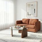 Modern living room with brown sofa, glass coffee table, and abstract art on white wall.